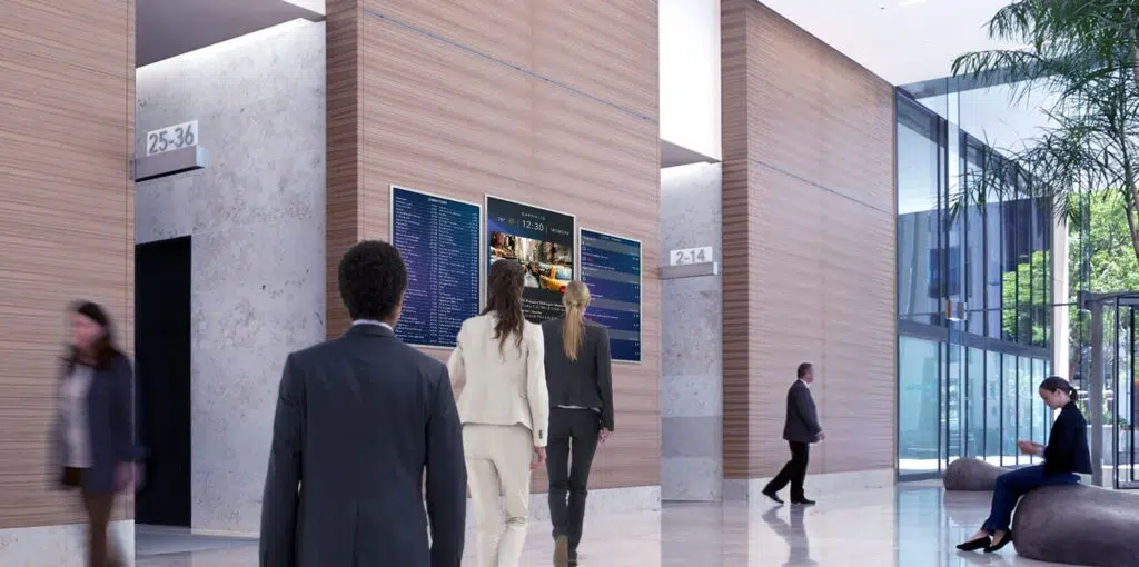 several young professionals view a OOH ad by reading digital signage in a building lobby