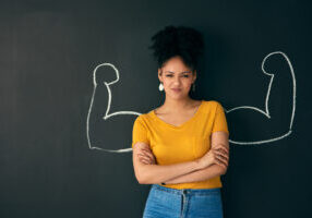 Shot of a woman posing with a chalk illustration of flexing muscles against a dark background